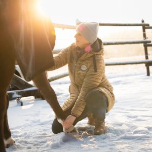 Photo of woman doing the Scapula Release Masterson Method technique with a blanketed horse outside in the winter.