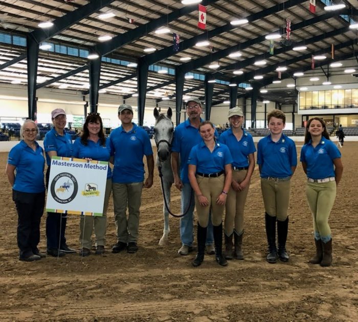 USPCFestival2021GroupPhoto Photo of people in a large arena with a horse and a Masterson Method banner.