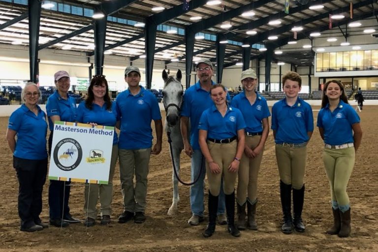 Photo of people in a large arena with a horse and a Masterson Method banner.