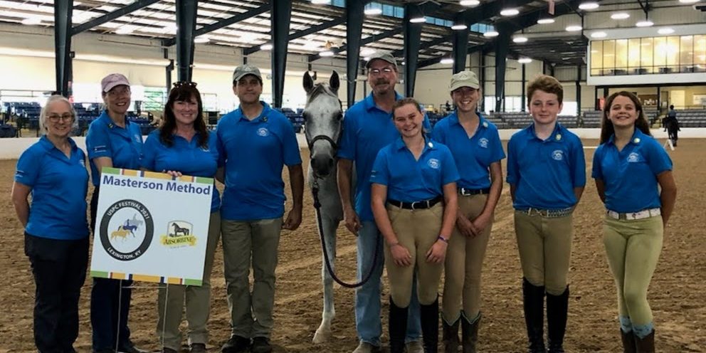 Photo of people in a large arena with a horse and a Masterson Method banner.