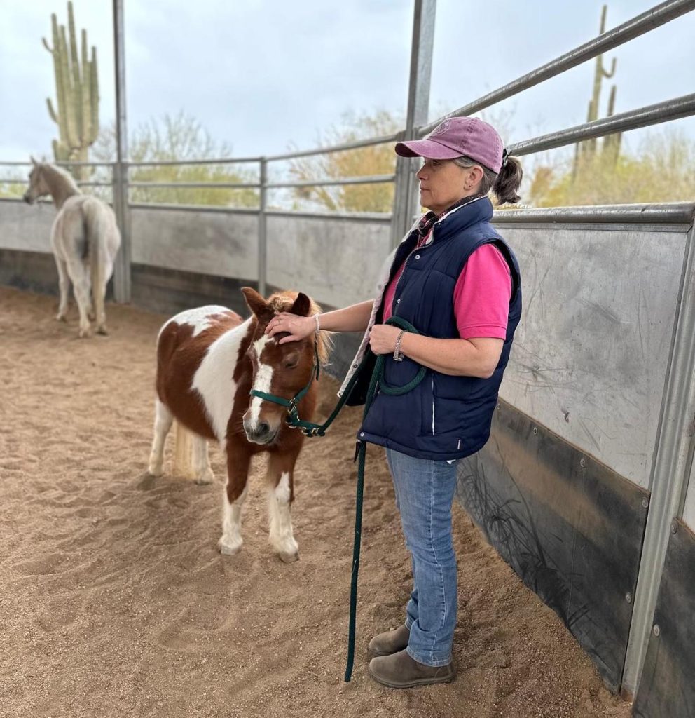 Photo of Vicky holding hand on forehead of miniature horse.