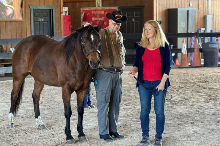 Photo of man resting his hand on horse's poll and woman holding lead rope.