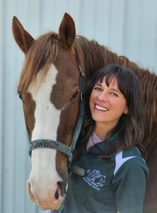A woman, smiling, with a horse.