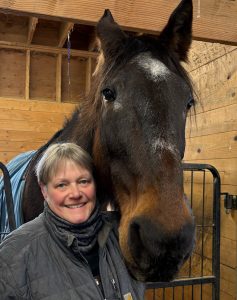 A woman smiling, with a horse.