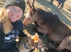 A woman smiling, with a horse and dog.