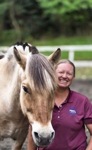 A woman, smiling, with her horse.
