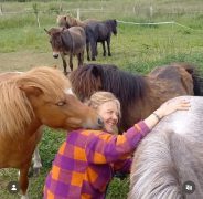 A woman laughing with horses surrounding her.