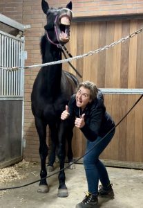 A woman giving thumbs up to yawning horse.